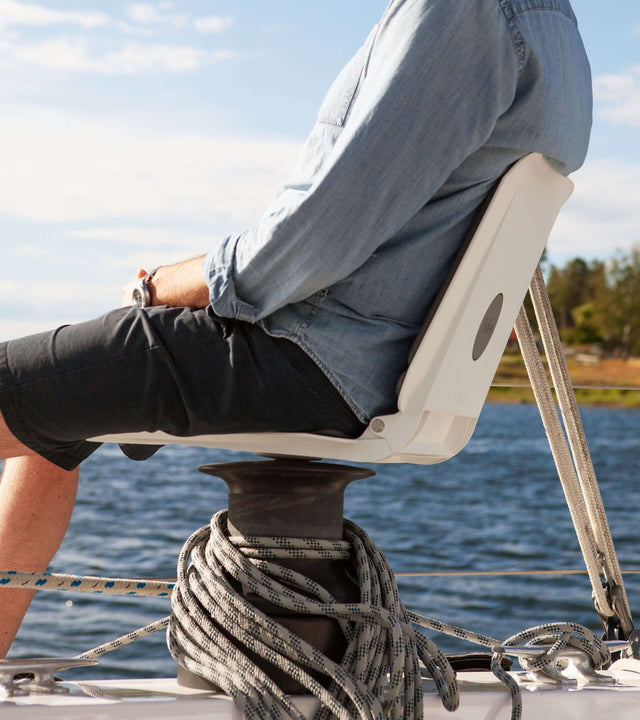 A person sitting on a portable winch seat for sailboat, enjoying comfort on the water with ropes and a scenic view.