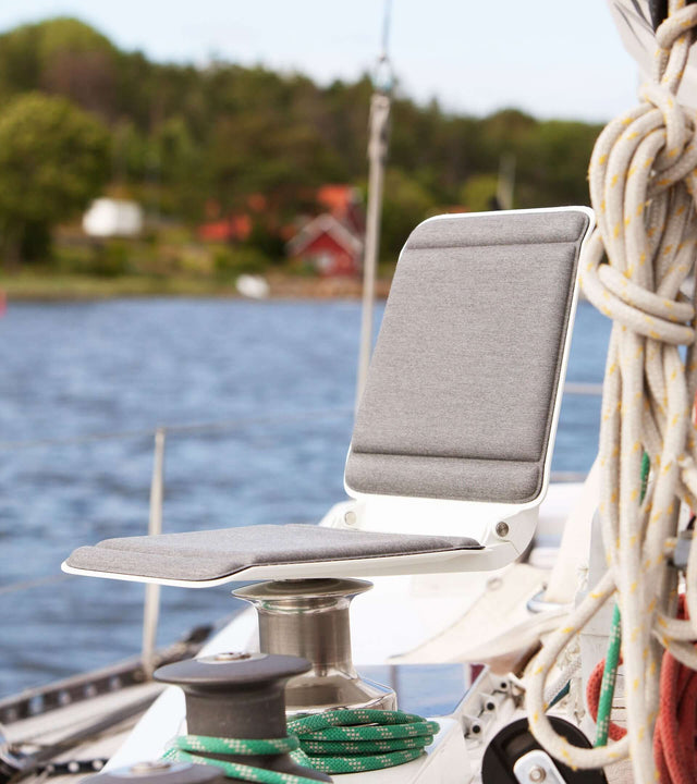 Portable winch seat for sailboat positioned near water, showcasing comfort and functionality on a sailboat.