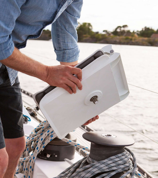 Person holding a portable winch seat for sailboat while on deck, ready to enhance onboard comfort.
